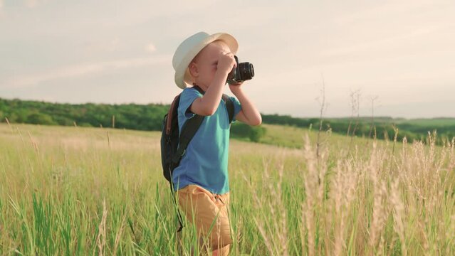 Happy boy dreams of becoming photographer. Kid plays in park in summer, spring. Cute little kid is holding vintage camera and taking pictures of nature. Child dreams of traveling, making discoveries
