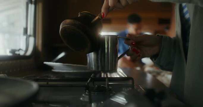 Women's hands pour coffee from a Turkish cup into a mug, a man plays guitar sitting on a bed in the background. Romantic van ride