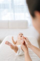 Vertical high-angle view of loving mother massaging newborn infant baby feet with thumbs tender...