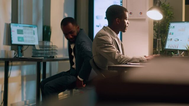 Funny worker distracting colleague during nightshift, bumping into him using desk chair. Happy coworkers racing eachother to avoid tediousness during overnight stay in office