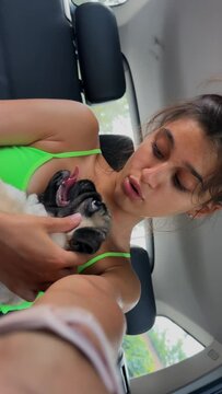 With her pug dog in her arms, a sporty young girl is inside the car, wearing sports clothing.