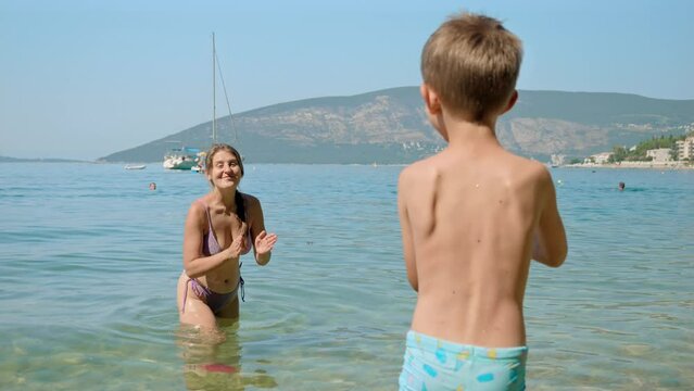 Slow motion of happy mother with son playing frisbee on the sea beach. Family holiday, vacation and fun summertime of children and parents