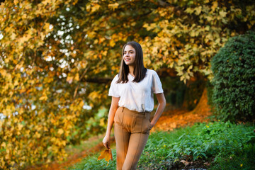 Autumn woman with fall yellow maple leaf, outdoor portrait. Beautiful model with autumn leaves, fall yellow maple in autumnal park. Autumn girl enjoying warm sunny weather in autumn fall season.