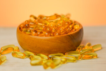 omega fatty acids oil capsules in a wooden cup on a blurred orange background.Fish oil jelly...