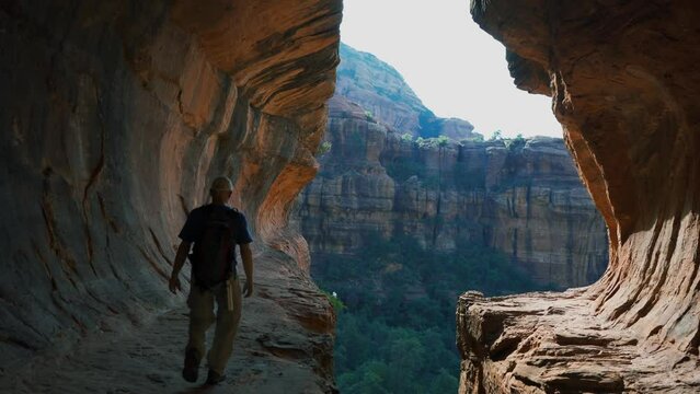 A man exploring a sandstone cave above a scenic valley