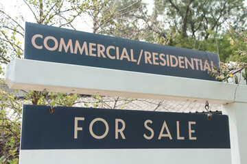 commercial residential for sale sign on white wood post with trees and sky behind, white and blue...