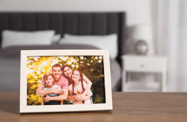 Fototapeta na wymiar Frame with family photo on wooden table in bedroom, space for text
