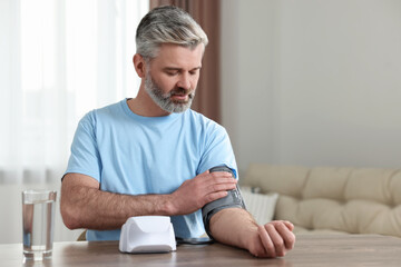 Man measuring blood pressure at table indoors