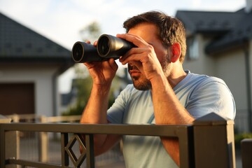 Fototapeta na wymiar Concept of private life. Curious man with binoculars spying on neighbours over fence outdoors