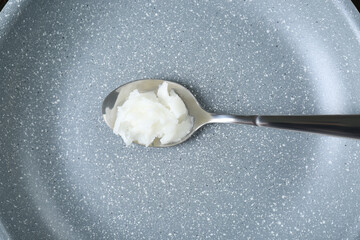 Organic coconut cooking oil and spoon on frying pan, top view