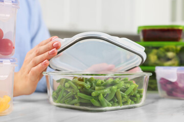 Woman sealing container with green beans at white marble table in kitchen, closeup. Food storage