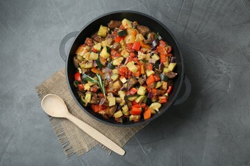 Delicious ratatouille in baking dish and wooden spoon on grey table, flat lay