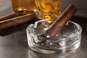 Smoldering cigar, ashtray and whiskey on grey table, closeup