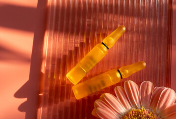 Two orange ampules with serum, vitamins or other cosmetic products inside on pink background with...