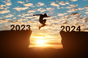 Happy new year 2024 concept. Silhouette of man jump on the cliff between 2023 to 2024 years over...