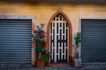 Fototapeta na wymiar Facade of a building with potted plants on the side of doors with metal safety shutters