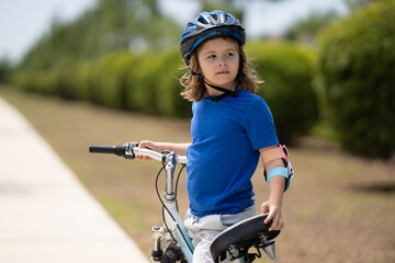 Naklejka premium Little kid boy ride a bike in the park. Kid cycling on bicycle. Happy smiling child in helmet riding a bike. Boy start to ride a bicycle. Sporty kid bike riding on bikeway. Kids bike.
