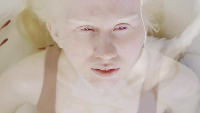 From above view close-up portrait of young woman with albinism relaxing in water with small fish