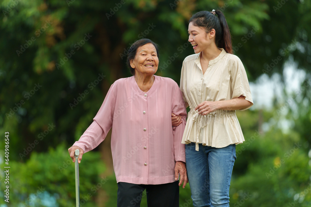 Wall mural happy granddaughter and senior woman with walking stick in the grass field at park