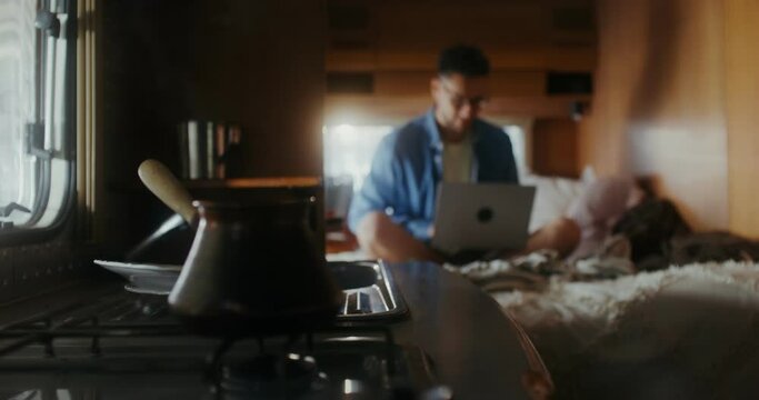 A young man with glasses uses a laptop sitting on a bed, traveling on a RV