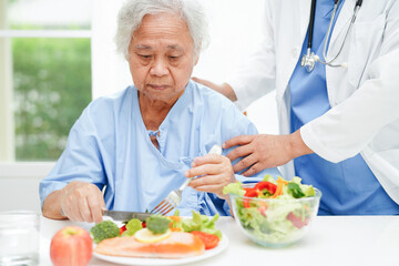 Asian elderly woman patient eating salmon stake and vegetable salad for healthy food in hospital.
