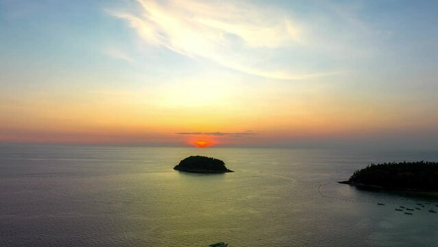 .Aerial hyperlapse The sun slowly sets over the horizon in the ocean.The sky is painted with streaks of yellow and orange..The fading light casts a gentle glow on the waves.Pu island in the vast sea.