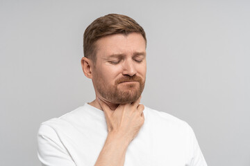 Obraz premium Unhappy male patient with severe sore throat. Sick upset man clutching writhing in pain touching neck, isolated on studio background. Cold symptoms, tonsillitis, viral diseases requiring treatment. 