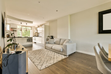 a living room with wood flooring and white furniture in the center of the room is an open kitchen area