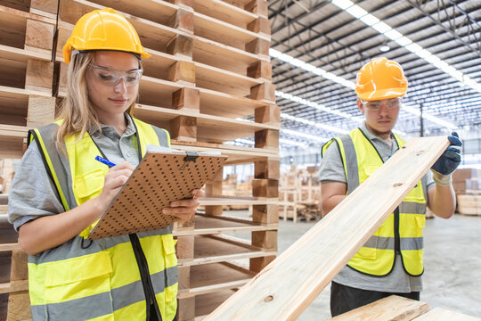 Team engineer carpenter wearing safety uniform and hard hat working holding clipboard checking quality of wooden products at workshop manufacturing. man and woman worker wood warehouse industry.
