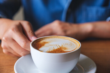 Closeup image of a woman holding a cup of latte coffee on the table