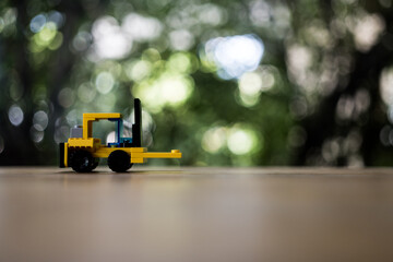 Yellow toy forklift loader on nature background with copy space for text. Moving service and distribution products. Delivery production. Logistics and industrial concept.