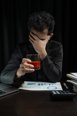 Asian businessman stressed at work failed business problem paperwork Desperate man holding a glass of alcohol Sitting at the desk late at night in the office Depressed and hopeless concept.