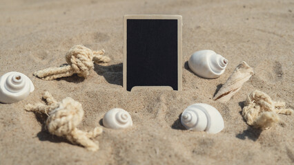 Empty blackboard frame board with copy space for your text or design displays on sandy beach. Starfish and shells decoration. Summer vacation and holiday business travel concept. Template Mock up for