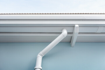 Rain gutter install on steel structure, connect to pvc downpipe or downspout, elbow at eaves, exterior house building. Also called guttering or eavestrough for water drainage system. Look new clean.