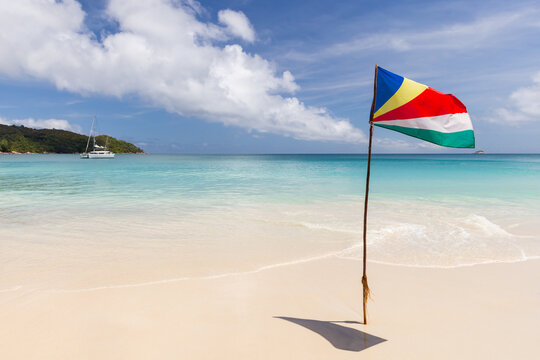 The flag of Seychelles mounted on the beach waving in wind on a sunny day
