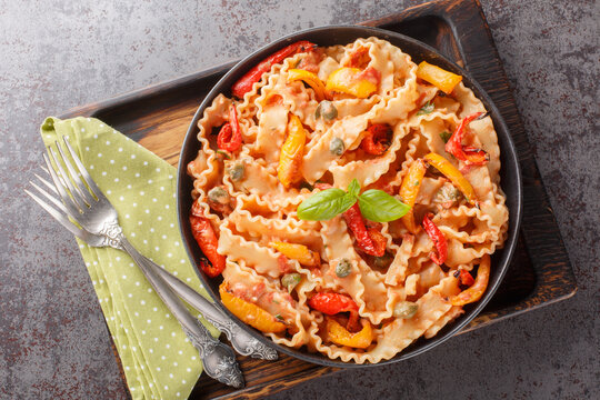 Mafaldine also known as reginette or simply mafalda or mafalde pasta in Creamy Tomato Sauce with capers and baked papper closeup on the plate on the table. Horizontal top view from above