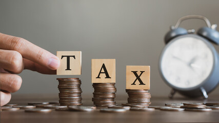 Tax time concept.Hand holding wooden block with TAX word and clock background.Tax...
