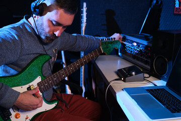 Musician man tuning his electric guitar with mixing console at home recording studio. Music...