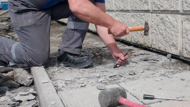 Slow motion video. Worker repairs foundation of building outside on summer day. Hands of bricklayer with hammer and chisel during work.
