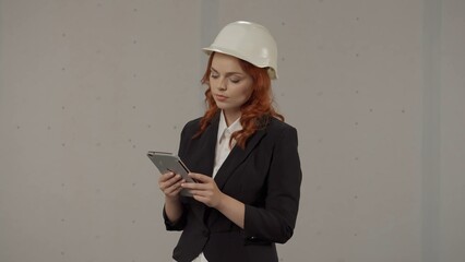 A woman architect takes notes in the tablet. Business woman in a protective helmet and with a tablet on a gray background in the studio.