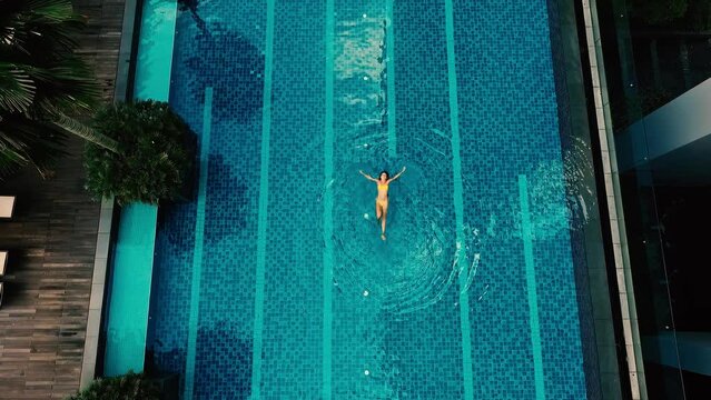 Aerial view of a woman in yellow swimsuit swimming in the pool. Summer lifestyle