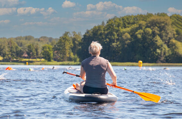A woman paddles on SUP boards on a large river during a swimmers' race. Stand up paddle boarding is...