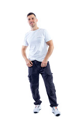 Fototapeta premium A smiling handsome man stands in a white t-shirt and dark trousers and holds his hands in his pockets. Success, positive and energy. Isolated on white background. Vertical. Space for text. 