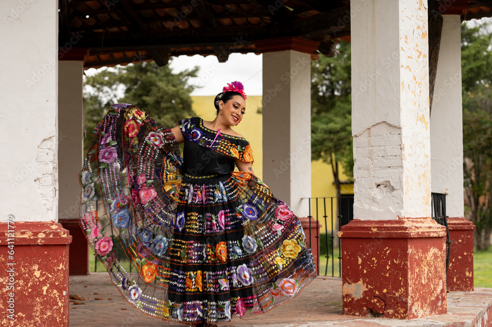 Wall mural Mexican folk dancer woman from the state of nayarit, Mexican pink nayarrita folk costume with blue, fan and dancing with skirt and turns on black background