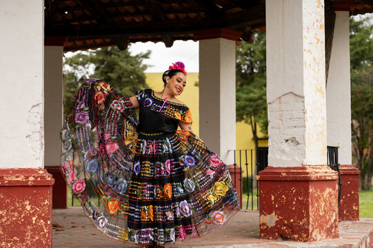 Mexican folk dancer woman from the state of nayarit, Mexican pink nayarrita folk costume with blue, fan and dancing with skirt and turns on black background