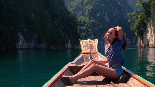 Lifestyle video of pretty travel woman sitting in wood long tail boat on tropical limestone cliffs . Explore and vacation concept. Khao Sok lake, Thailand.