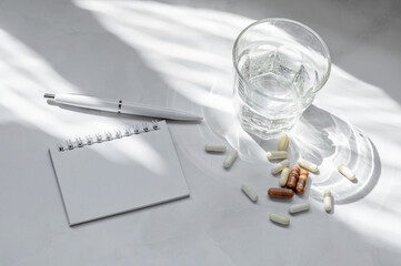 Pills and capsules, glass with pure water, blank notebook mockup, on white table background with...