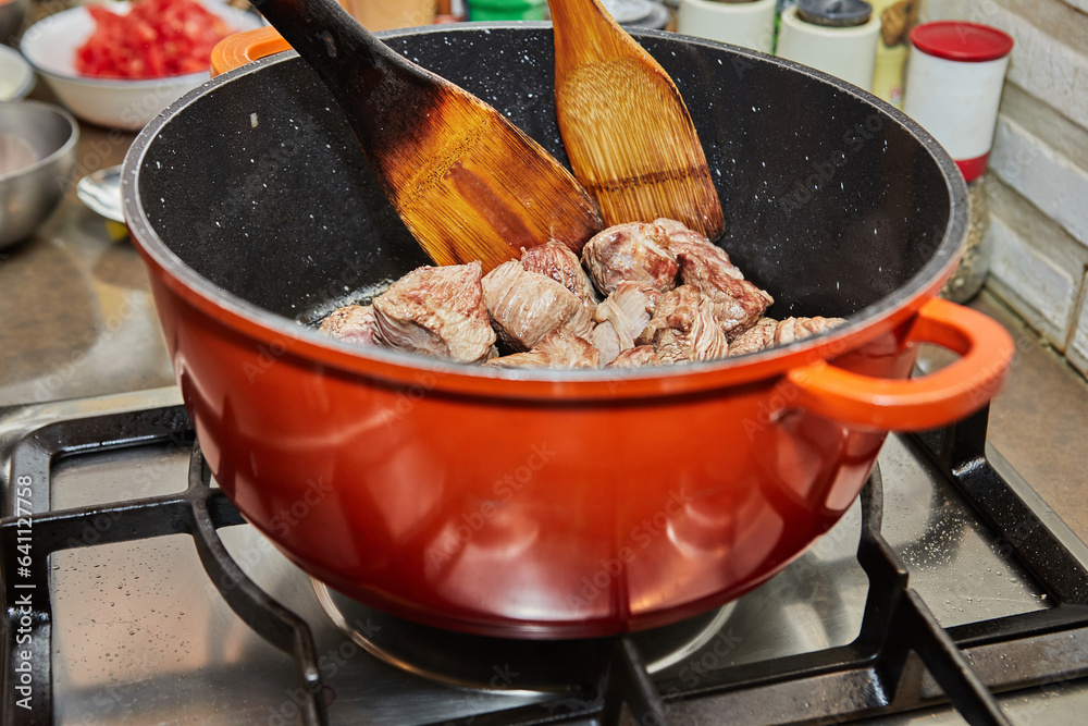 Poster Pieces of beef are fried in pan on gas stove. Wooden sticks for stirring