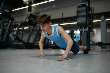 Naklejka na ściany i meble Teenager healthy boy making gymnastics pushup while training at gym