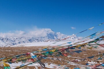 Mt. Shishapangma, its peak engulfed in a snowstorm, with Tibetan prayer flags fluttering in the foreground. Captured from the Tong La pass at 5,130 meters in Tibet.